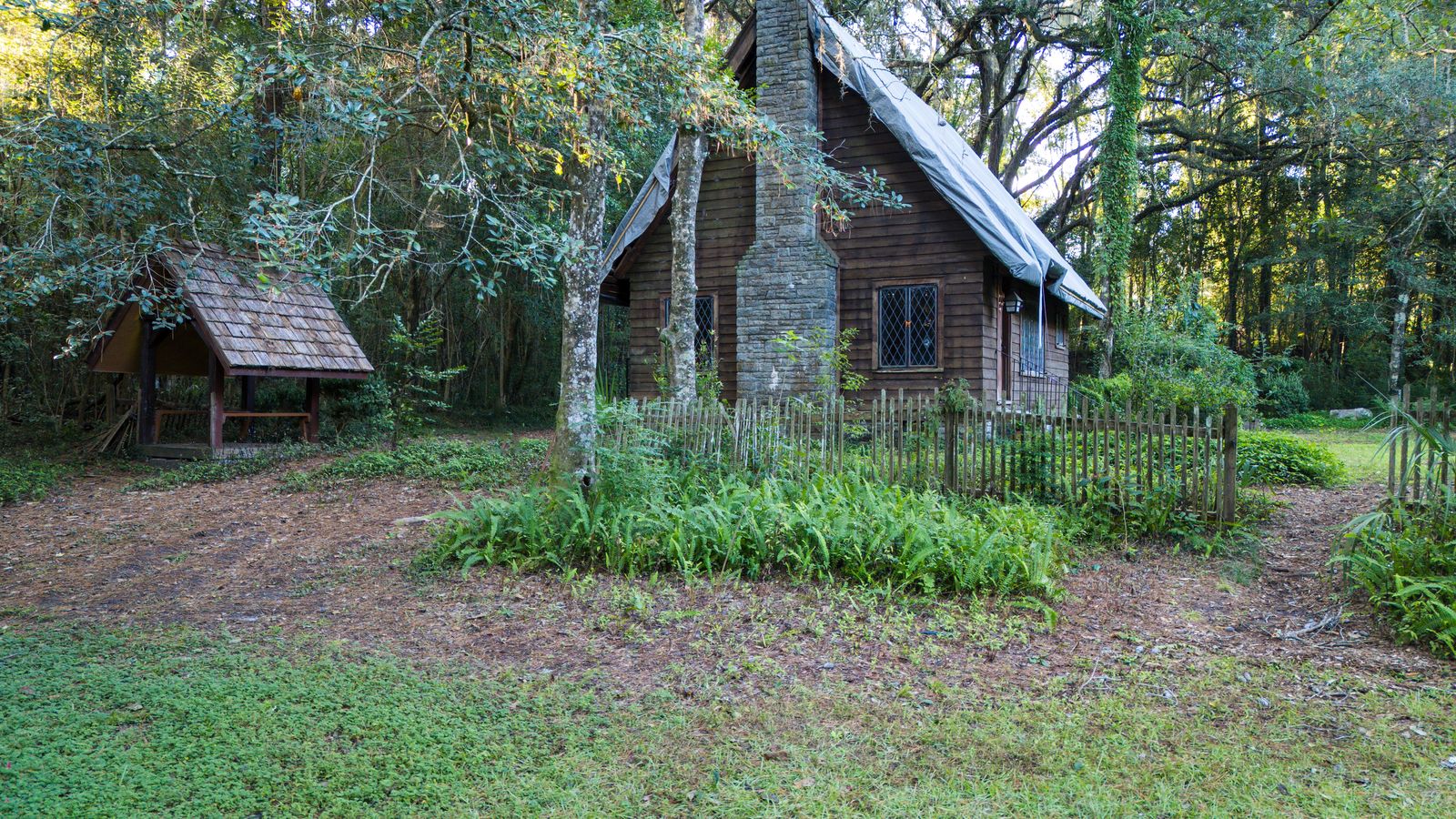 Rustic wooden cottage with a stone chimney and picket fence in the woods at Lichgate on High Road