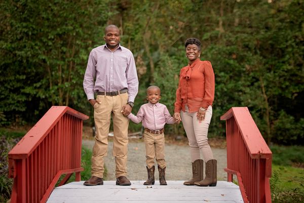 Family of three standing on a red footbridge surrounded by greenery at Dorothy B. Oven Park