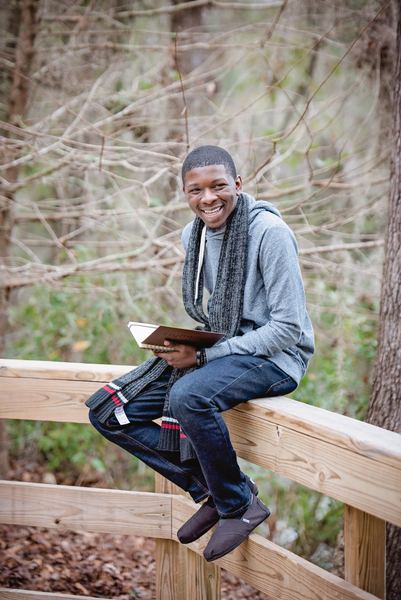 Teen sitting on a wooden bridge railing with a book at Dorothy B. Oven Park