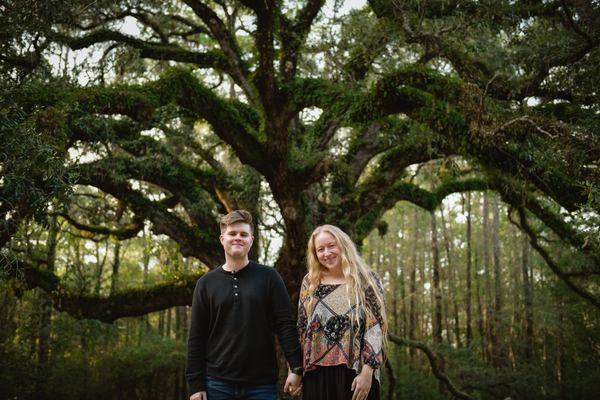 Engaged couple standing together under the oak canopy at Lichgate