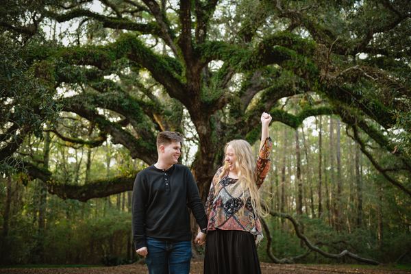 Newly engaged couple celebrating with a raised hand beneath the Lichgate oak