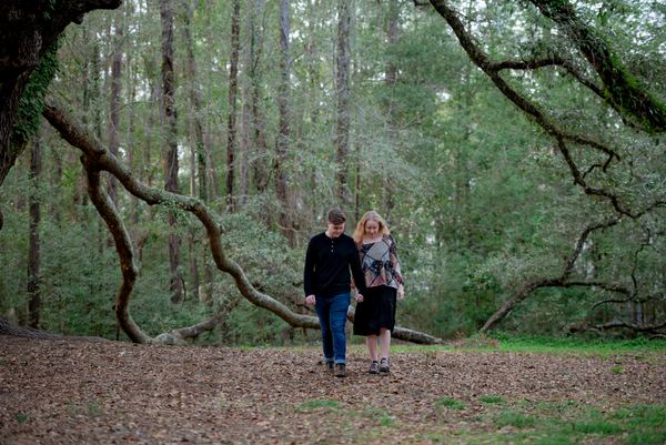 Couple walking among pines and sweeping oak limbs at Lichgate
