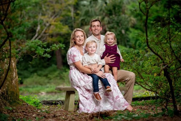 Family of four gathered on a bench among lush garden greenery at Maclay Gardens in Tallahassee