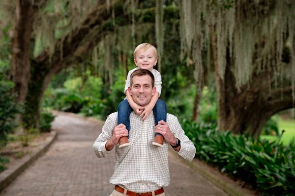 Father carrying his young son on his shoulders along an oak-lined brick path at Maclay Gardens in Tallahassee