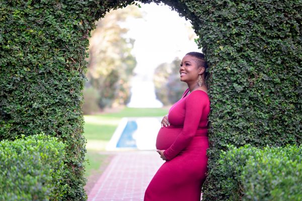Maternity portrait in a magenta gown beside a clipped hedge archway at Maclay Gardens in Tallahassee