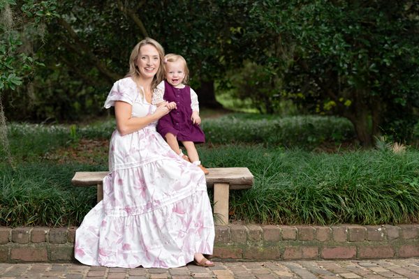 Mother in a floral dress sitting with her toddler daughter on a garden bench at Maclay Gardens, Tallahassee