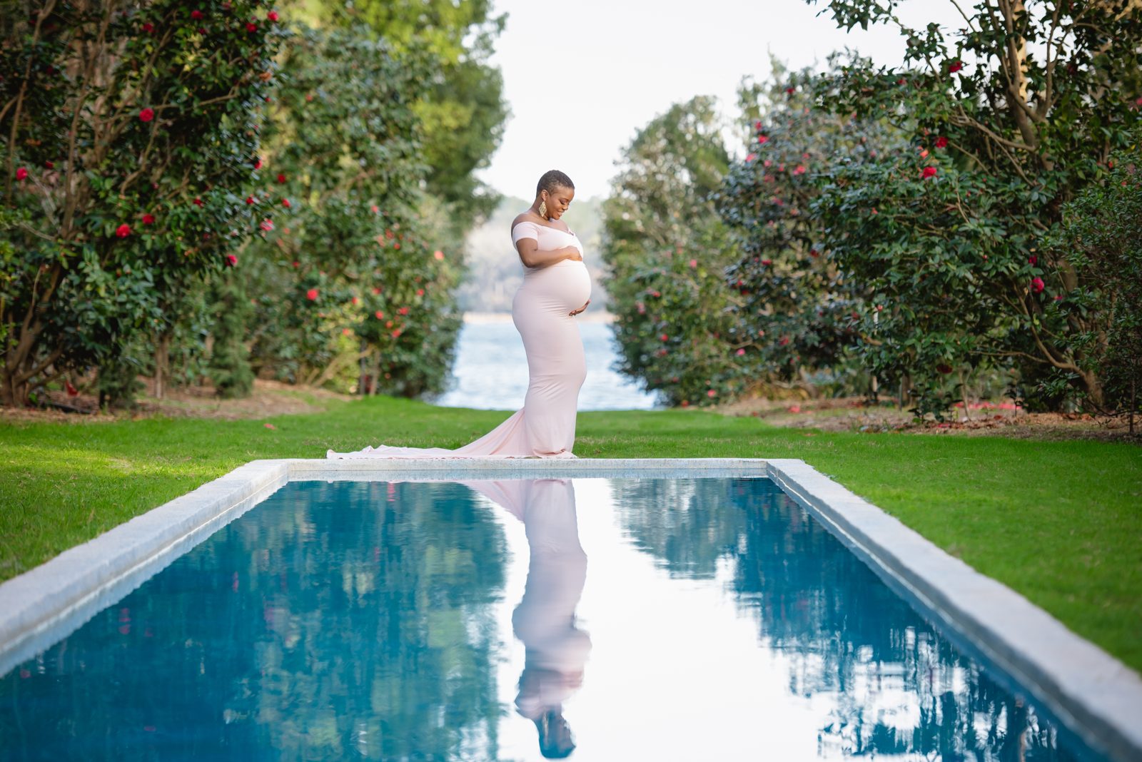 Expectant mother in a light gown standing at the end of the long reflecting pool at Maclay Gardens in Tallahassee