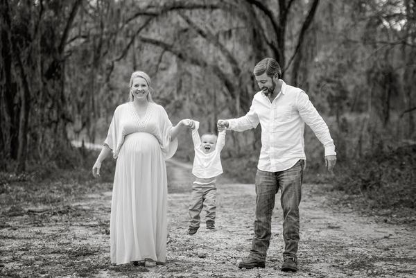 Black-and-white photo of parents swinging their child along a wooded path at Millers Landing