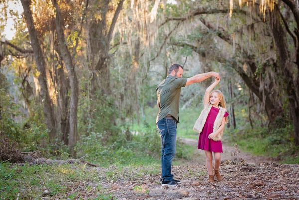 Father twirling his daughter under moss-draped oaks at Millers Landing