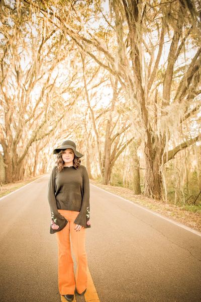 Woman in a hat and orange pants standing on the oak canopy road at Millers Landing