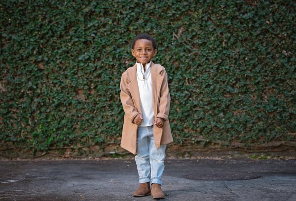 Young boy in a tan coat standing in front of an ivy-covered wall at Pebble Hill Plantation