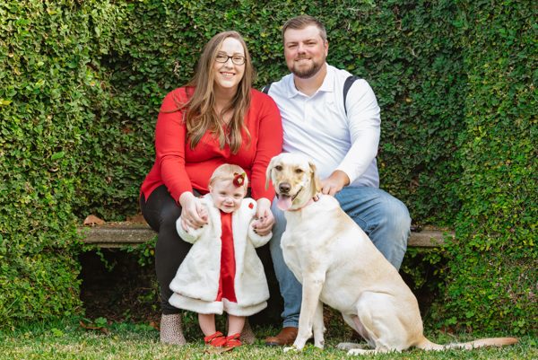 Family with their toddler and yellow Labrador on a bench before an ivy-covered wall at Pebble Hill Plantation, near Tallahassee