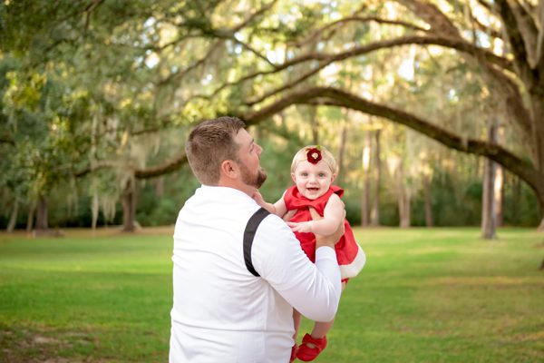 Father lifting his toddler daughter on a lawn under spreading live oaks at Pebble Hill Plantation