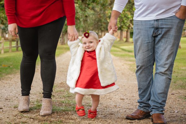 Toddler in a red dress holding her parents' hands on a garden path at Pebble Hill Plantation