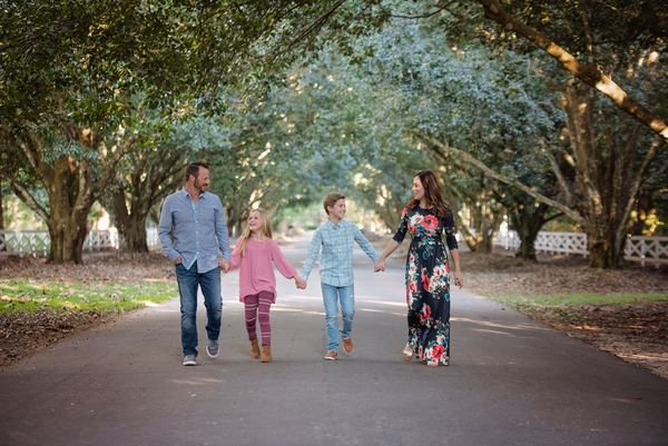Family of four walking hand in hand down an oak-tunneled drive at Rose Hill