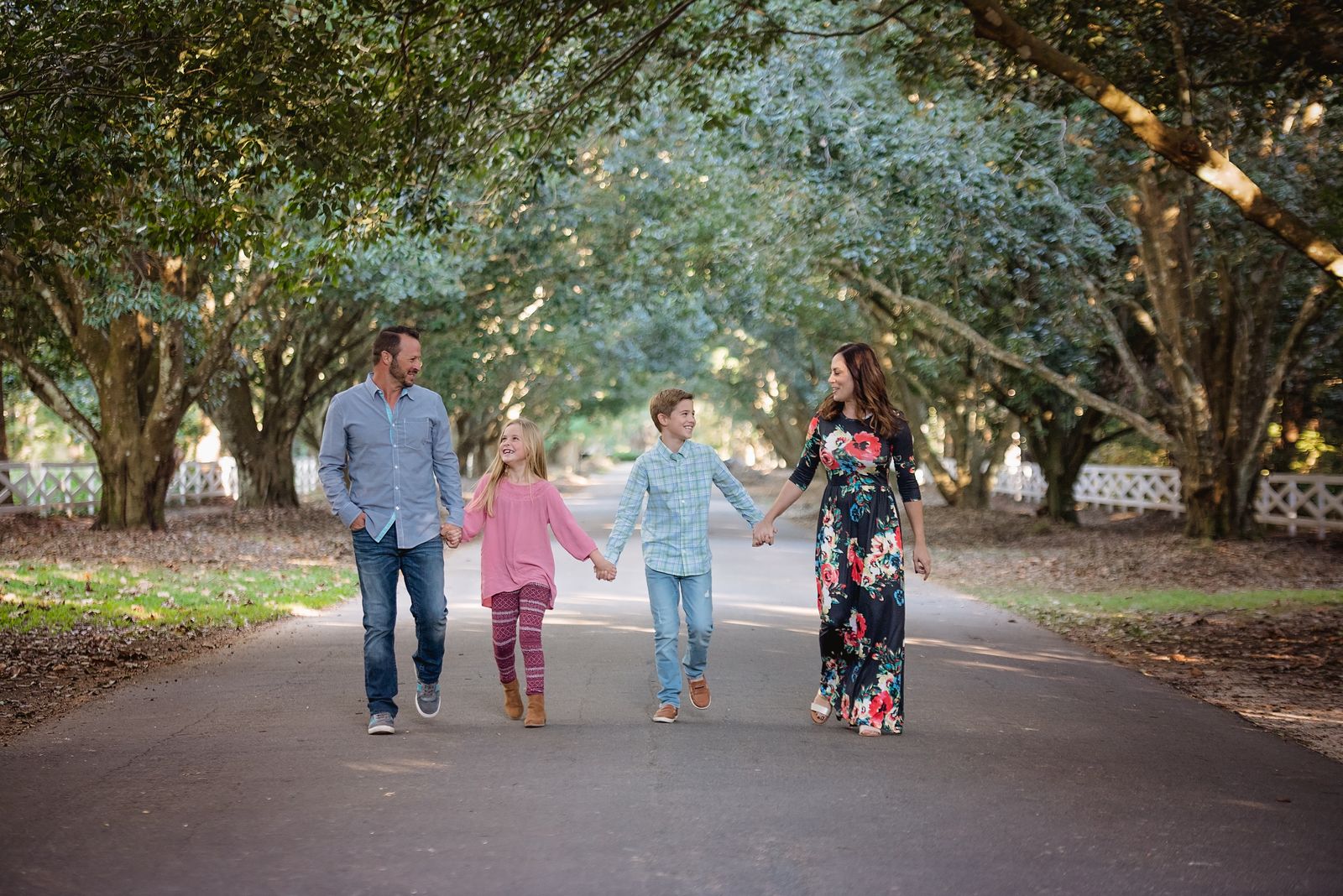 Family of four walking hand in hand down an oak-tunneled drive at Rose Hill