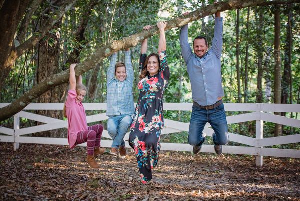 Family playfully hanging from an oak branch beside a white fence at Rose Hill
