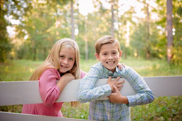 Brother and sister leaning on a white wooden fence in golden light at Rose Hill