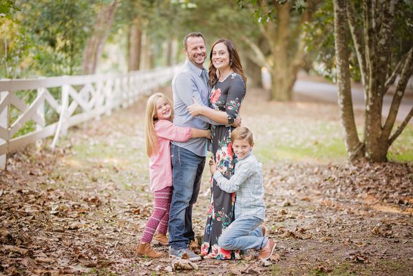 Family hugging by a white fence on a leaf-covered path at Rose Hill