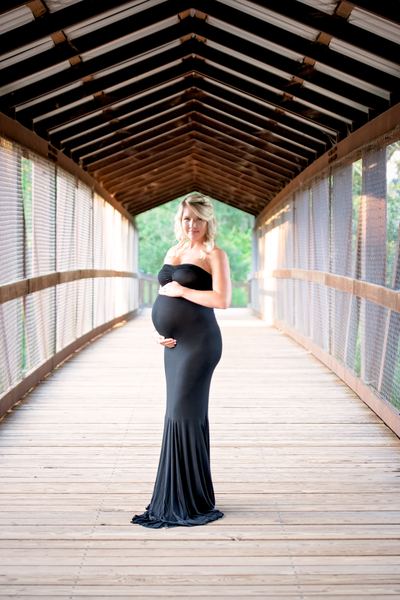 Maternity portrait framed by the peaked roof of the covered bridge at Tom Brown Park