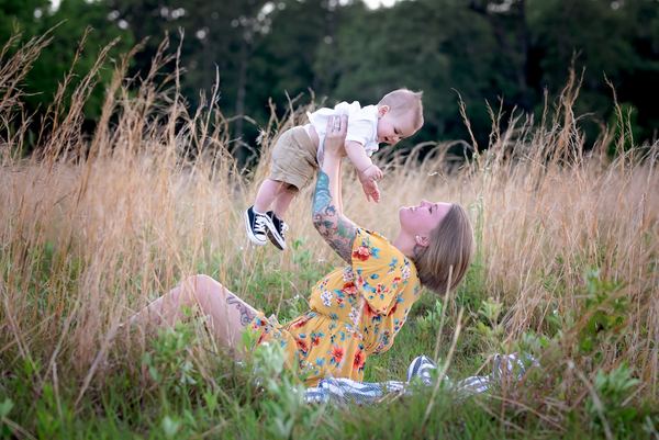 Mother lifting her baby overhead in a tall-grass meadow at the Alford Greenway