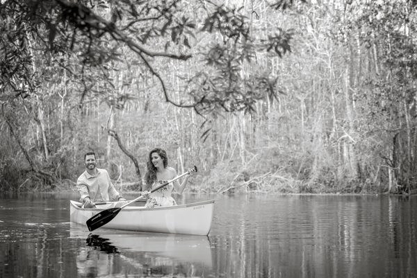Black-and-white photo of a couple paddling a canoe beneath moss-draped trees on the Wacissa River